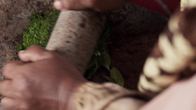 An Asian woman grinds leaves from the henna tree to make henna paste