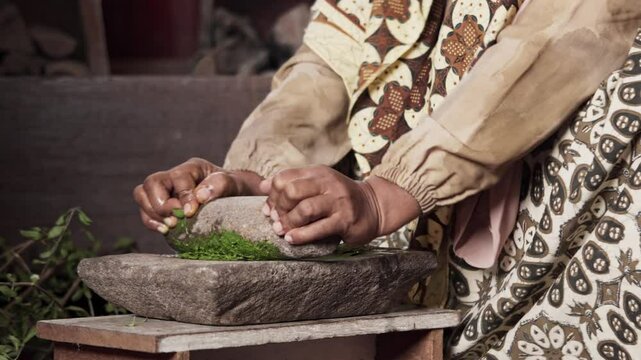 An Asian woman grinds leaves from the henna tree to make henna paste