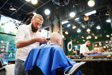 Barber using comb and shaver to cut hair. Professional hairdresser shaving little kid's nape.