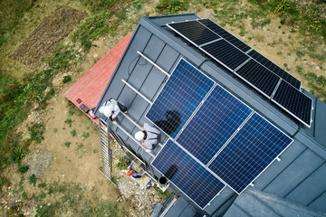 Men builders installing solar panel system on roof of house. Electricians in helmets lifting up...