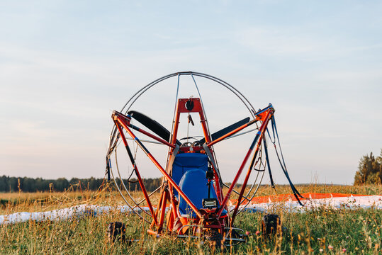 red paraplane with soft self-inflating wing stands set in field before the flight in sky above fields in countryside in summer at sunset