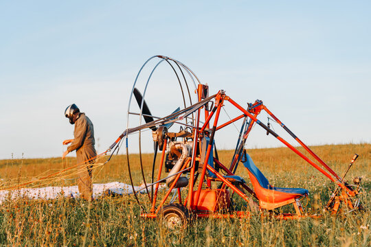 Paraglider man lays out soft self-inflating wing before the flight, preparing to fly on red paraplane in sky above fields in countryside in summer at sunset