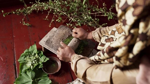 An Asian woman grinds leaves from the henna tree to make henna paste