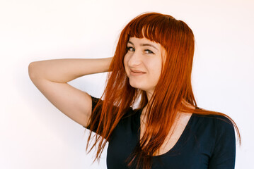 Obraz premium Young woman with long red hair smiling against a white background. A cheerful young woman poses playfully with her long red hair styled