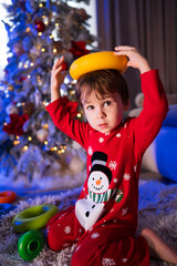 Young child playing with colorful toys near a decorated Christmas tree. A child dressed in festive pajamas joyfully plays with toys by a Christmas tree filled with lights.