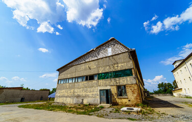Obraz premium Abandoned industrial building under a bright blue sky with clouds. An old warehouse stands empty against a vibrant blue sky, showcasing its deteriorating exterior and surrounding landscape.