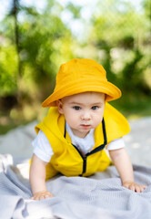 Baby crawling in a yellow outfit on a sunny day in the park. A baby dressed in a bright yellow outfit crawls on a blanket outside under a sunny sky