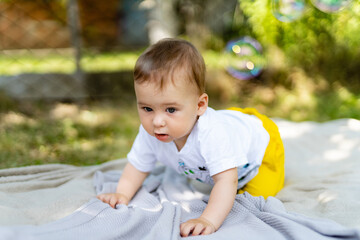 Baby crawling on a blanket in a sunny garden surrounded by bubbles. A baby is happily crawling on a...