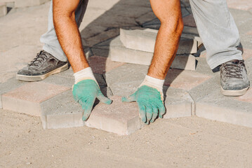 man worker in gloves lays asphalt tiles in sunny summer day, city improvement, city accomplishment concept