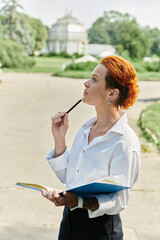 A woman in a white shirt, holding a notebook and a pen, looks up and contemplates on a sunny day.
