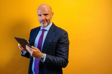 A man in a blue suit using a tablet in front of a yellow wall.