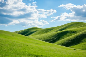 Obraz premium A large, grassy hillside with a clear blue sky. The sky is dotted with clouds, giving the scene a peaceful and serene atmosphere