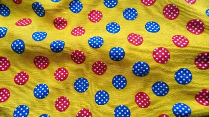 Fototapeta premium Bright yellow fabric with cheerful red and blue polka dots.