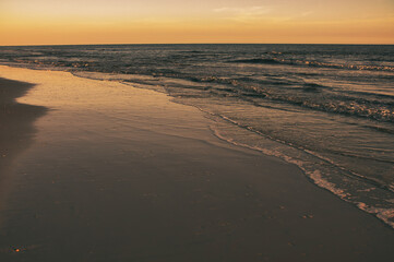 beautiful sunset along beach as waves roll in and out over warm reflecting sand. Tranquil and scenic view of vacation destination.