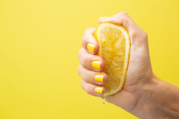 A woman's hand with yellow fingernails squeezing half a lemon.