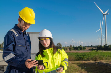 Two engineers working and holding the report at wind turbine farm Power Generator Station on mountain,Thailand people,Technician man and woman discuss about work