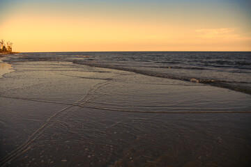 beautiful sunset along beach as waves roll in and out over warm reflecting sand. Tranquil and scenic view of vacation destination.