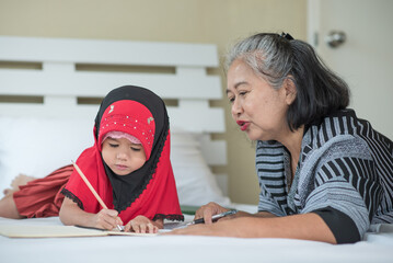 Young muslim girl writing a book with grandma, islamic child do homework at home