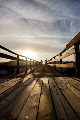 Naklejka premium Two children run along a wooden boardwalk bathed in the warm glow of the sunset. Capturing the essence of freedom, adventure and the beauty of nature.