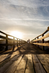 Obraz premium Two children run along a wooden boardwalk bathed in the warm glow of the sunset. Capturing the essence of freedom, adventure and the beauty of nature.