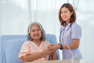 Obraz premium Asian female home nursing holding hand of older lady on the bed and encouraging patient