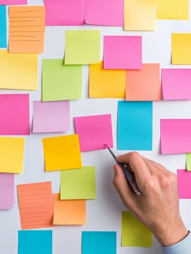 A hand points to a sticky note, suggesting a collaborative brainstorming session with colorful notes on a white board. This image is perfect for representing teamwork, innovation, ideas, and planning.