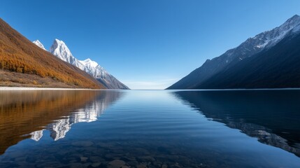 A tranquil scene of a pristine mountain lake, reflecting snow-capped peaks and vibrant autumn foliage. The calm water, blue sky, and distant mountains create a sense of peace and serenity.