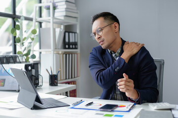 Stressed asian businessman suffering from neck pain while working on computer in office
