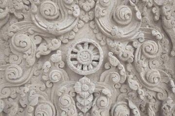 Detail of grey Dharmachakra Wheel sculpture with delicate etched floral design pattern on sandstone wall.Traditional Thai style stone craving at Wat Phu man fah temple, Buriram province, Thailand.