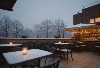An outdoor cafe with tables and chairs covered in snow on a snowy evening, with candles on the tables