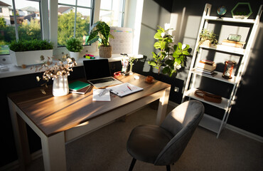 Modern, sunlit office desk is neatly arranged with laptop, documents, and coffee cup, surrounded by plants and personal items. Bright atmosphere and organized space reflect productivity and focus