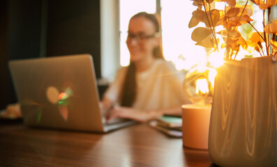 Soft focus shot of woman working on a laptop at a desk, with the warm glow of sunlight shining...