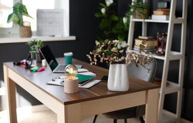 A modern, well-organized desk with a bulb, a vase, and various office supplies, including a laptop and notebooks. The sunlight streaming through the window creates a warm and productive workspace.