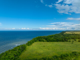 Aerial view of calm and wild Saka beach with a clear blue water on a cloudy summer day. Beautiful yellow and green fields and countryside road. Saka, Ida Viru county, Estonia. 