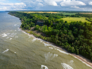 Aerial view of calm and wild Saka beach with a clear blue and yellow water on a cloudy summer day....
