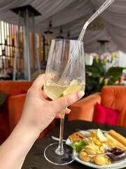 Woman holds summer cocktail with ice in bar or restaurant. Vertical