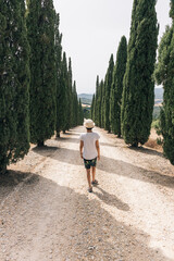 Girl with hat walking among pine trees, a typical landscape of Tuscany Italy