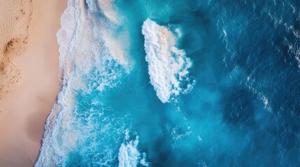 Aerial image of a brilliant blue sea on a clear, sunny day, featuring splashing waves and a sandy coastline
