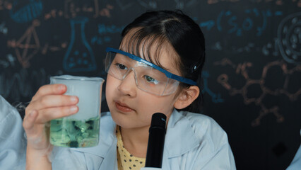 Young girl holding green chemical solution and inspect carefully while sitting in front of...