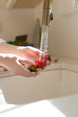 close up of a person washing strawberries backlit in kitchen white background