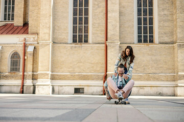 Fototapeta premium Playful young hipster couple having fun on skateboard on city street.