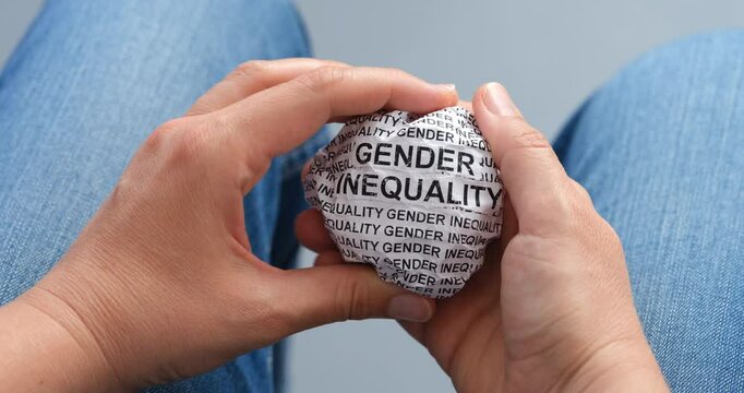 A woman is crumpling a paper ball with words Gender Inequality in her hands