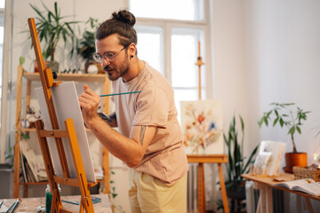 Skilled author painting with brush on easel at creative atelier.