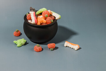 Colorful assortment of gummy Halloween candies in a black caldron bowl on a blue background