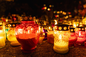 heart-shaped candle among glowing candles in the night at cemetery on all saints day, day of the dead, or memorial day