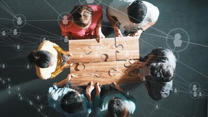 Top down view of business people gathering jigsaw together at meeting. Aerial view of diverse team collect or put piece of jigsaw puzzle together with computing global networking community. Symposium.