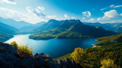 Fototapeta premium A breathtaking panoramic view of a tranquil lake nestled amidst towering mountains, with a clear blue sky and fluffy white clouds overhead. The scene embodies serenity, natural beauty, and the vastnes