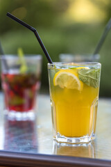 A glass of orange juice with a lemon slice in it sits on a table next to another