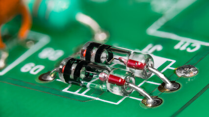 Two point-contact diodes in glass package on green printed circuit board. Closeup of electronic components with germanium crystal and metal wire semiconductor junction in striped tube on a PCB detail.