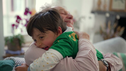 Obraz premium Grandfather embracing young boy in a warm hug, both smiling and laughing, highlighting a joyful and affectionate family moment in a cozy home environment